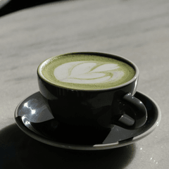 Foto matcha latte panas dengan latte art daun di cangkir hitam